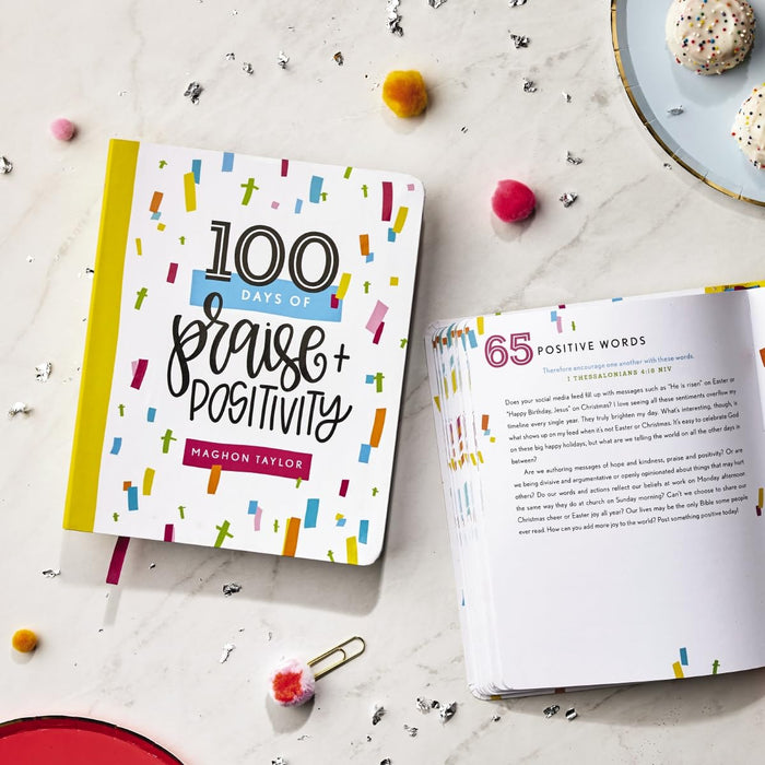 Book titled '100 Days of Praise + Positivity' by Maghon Taylor on a marble surface with decorative items.
