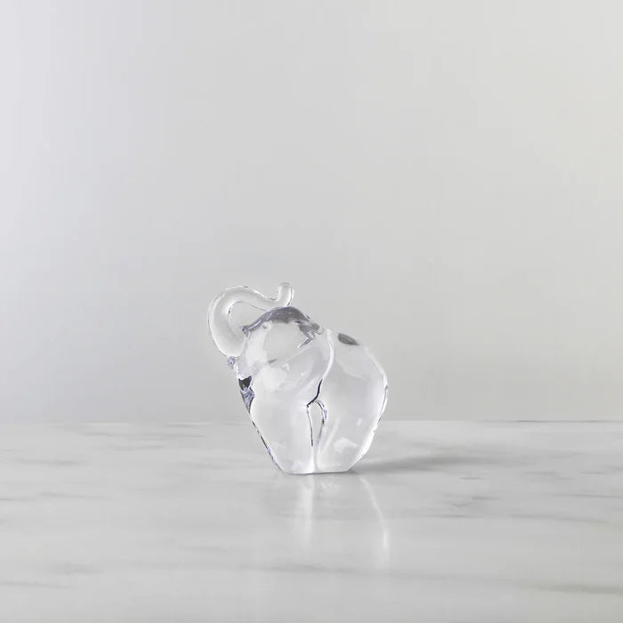 Clear glass elephant figurine on a light gray surface with a light gray background
