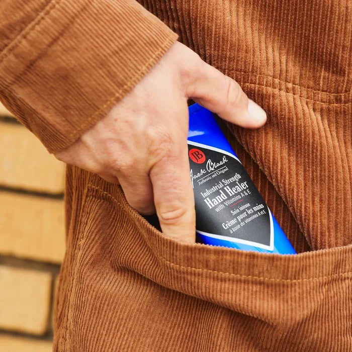Hand holding a bottle of hand cream in a brown jacket pocket with a blurred background