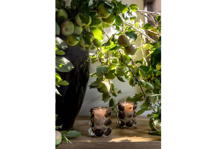 close up of large black vase with apple stems sticking out of it on a table.