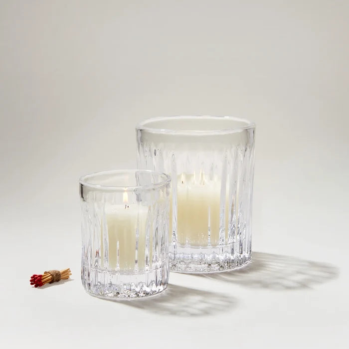 Two clear glass candle holders with lit candles on a light gray background