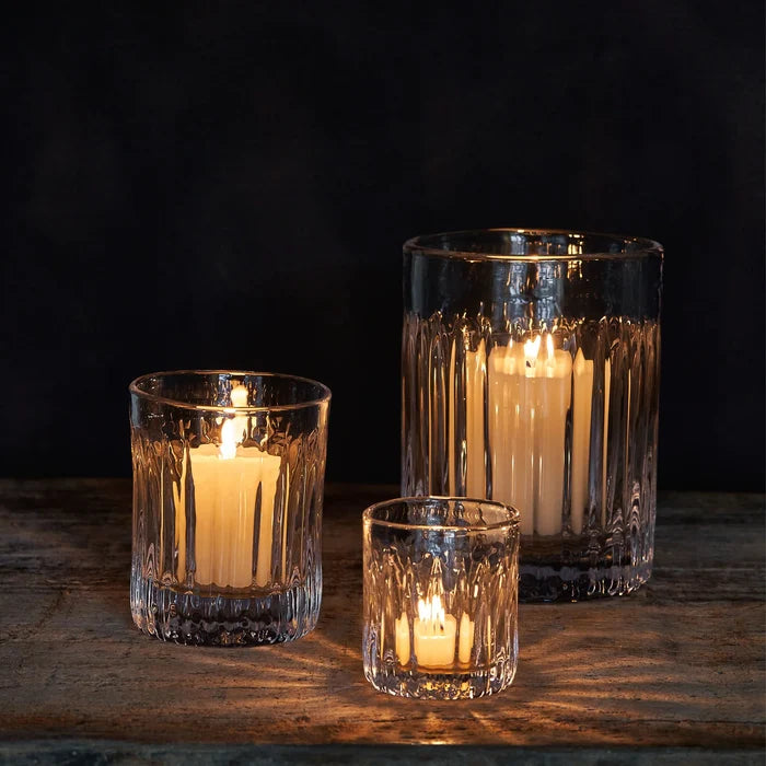 Three glass candle holders with lit candles on a wooden surface against a dark background