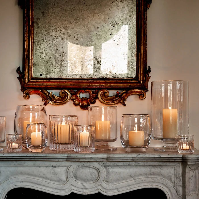 Decorative candles in glass holders on a mantelpiece with a mirror above.