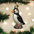 A glass puffin ornament hangs from a Christmas tree branch with blurred lights in the background.