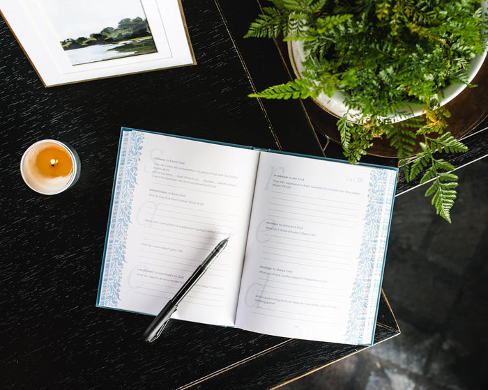 Open notebook with pen on a dark surface with a plant and candle