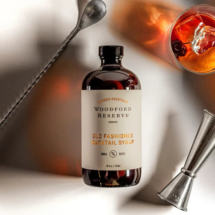 Woodford Reserve Old Fashioned Cocktail Syrup bottle with a cocktail and bar tools on a blurred background